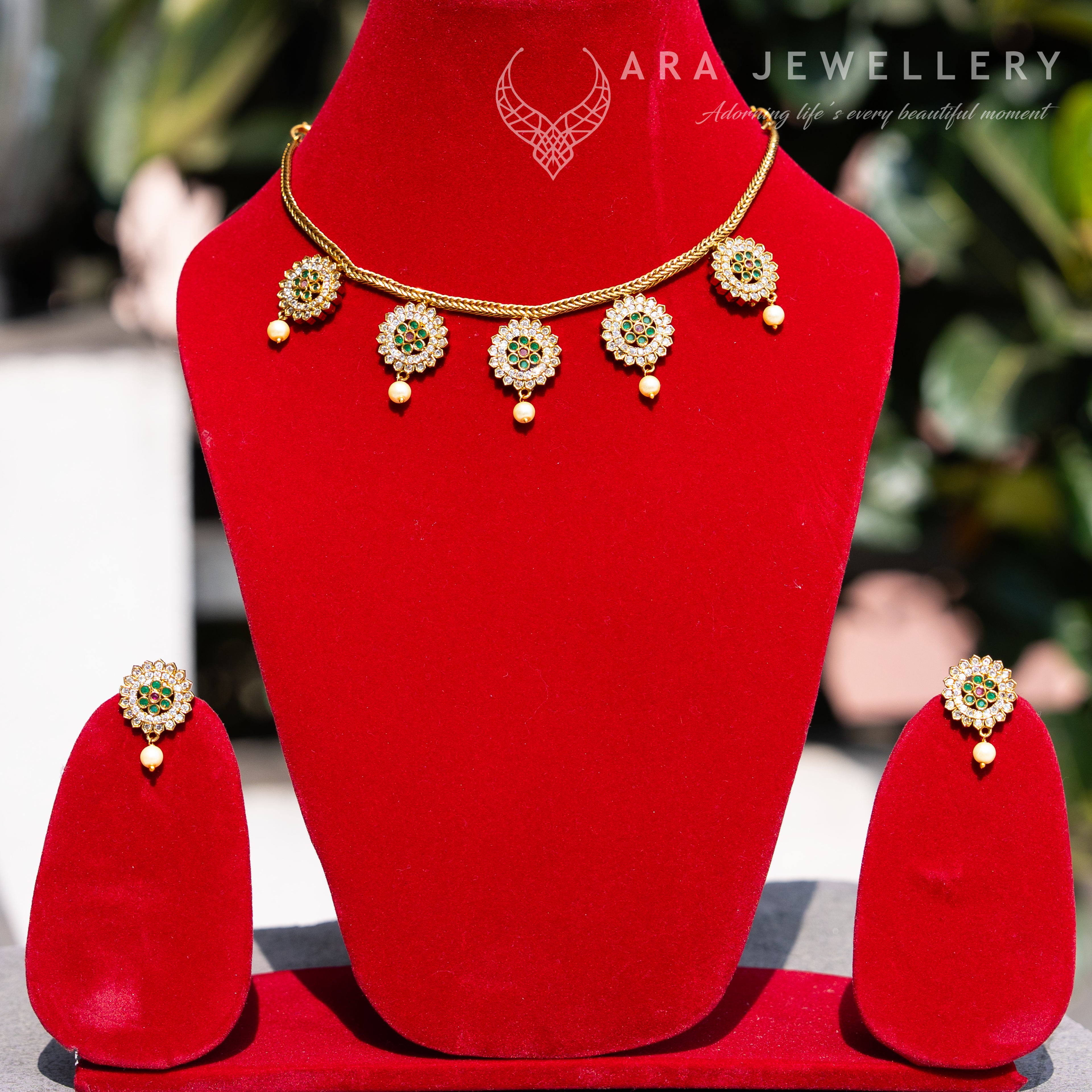 Jewellery set with necklace and earrings on a red stand, branded 'ARA Jewellery'.