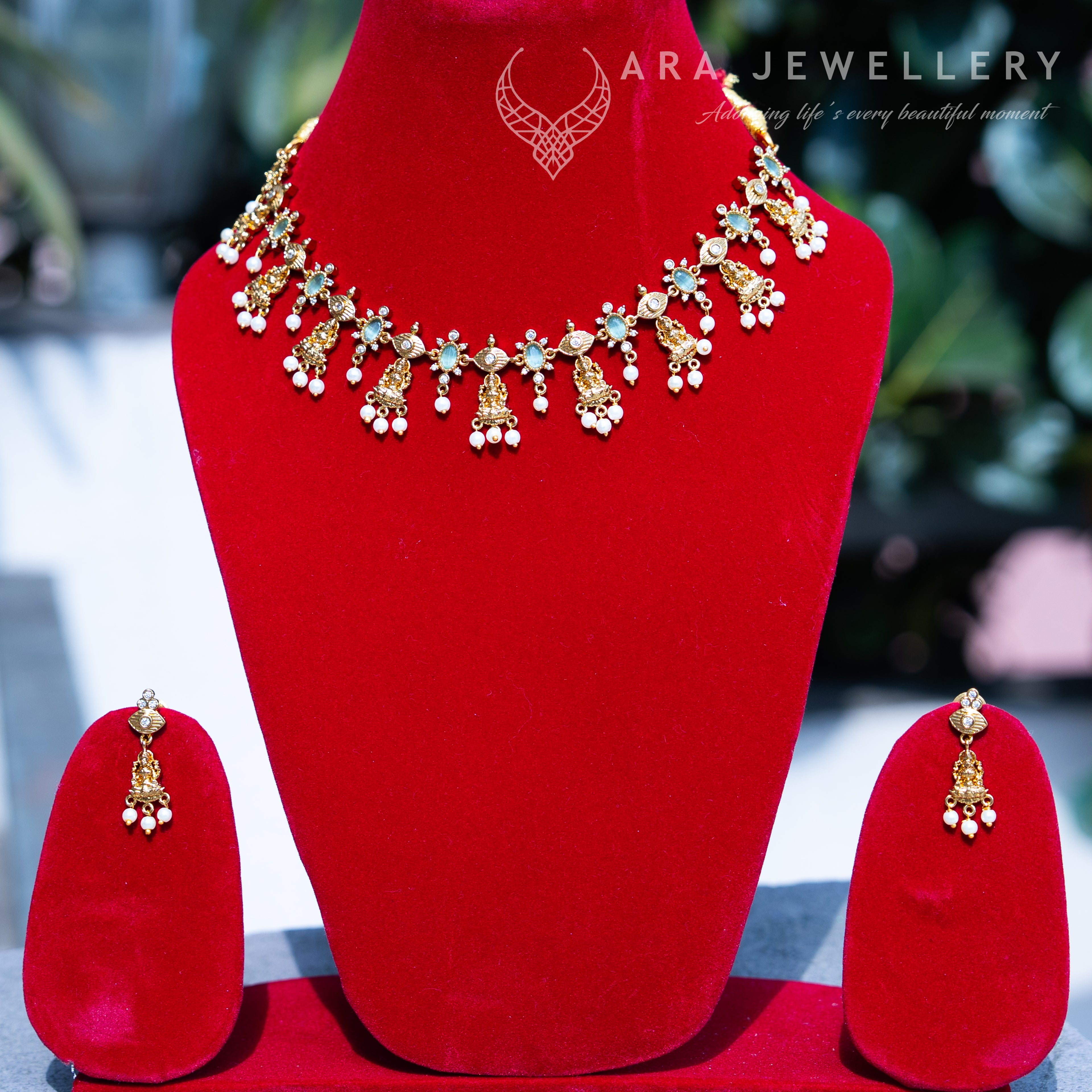Jewellery set with necklace and earrings on a red stand, branded 'ARA JEWELLERY'.